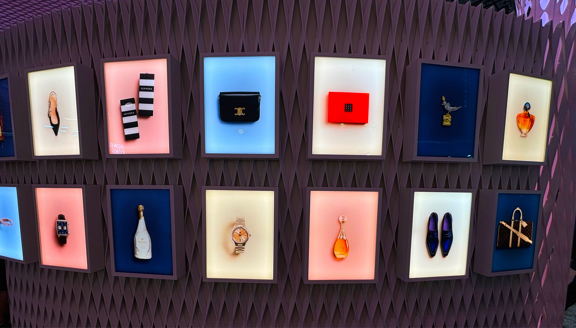 Backlit luxury retail display wall with designer accessories, Sephora boxes and Dom Ruinart bottle.