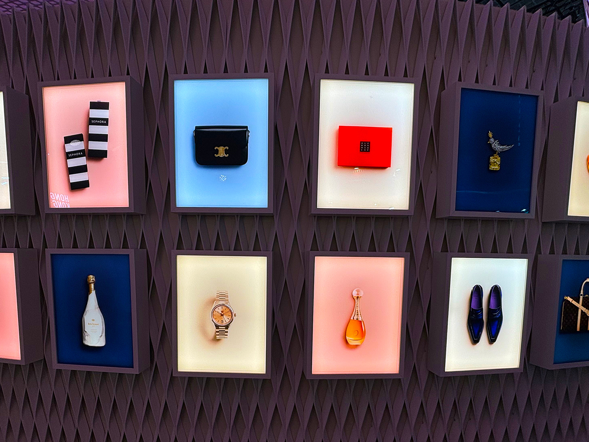 Backlit luxury retail display wall with designer accessories, Sephora boxes and Dom Ruinart bottle.