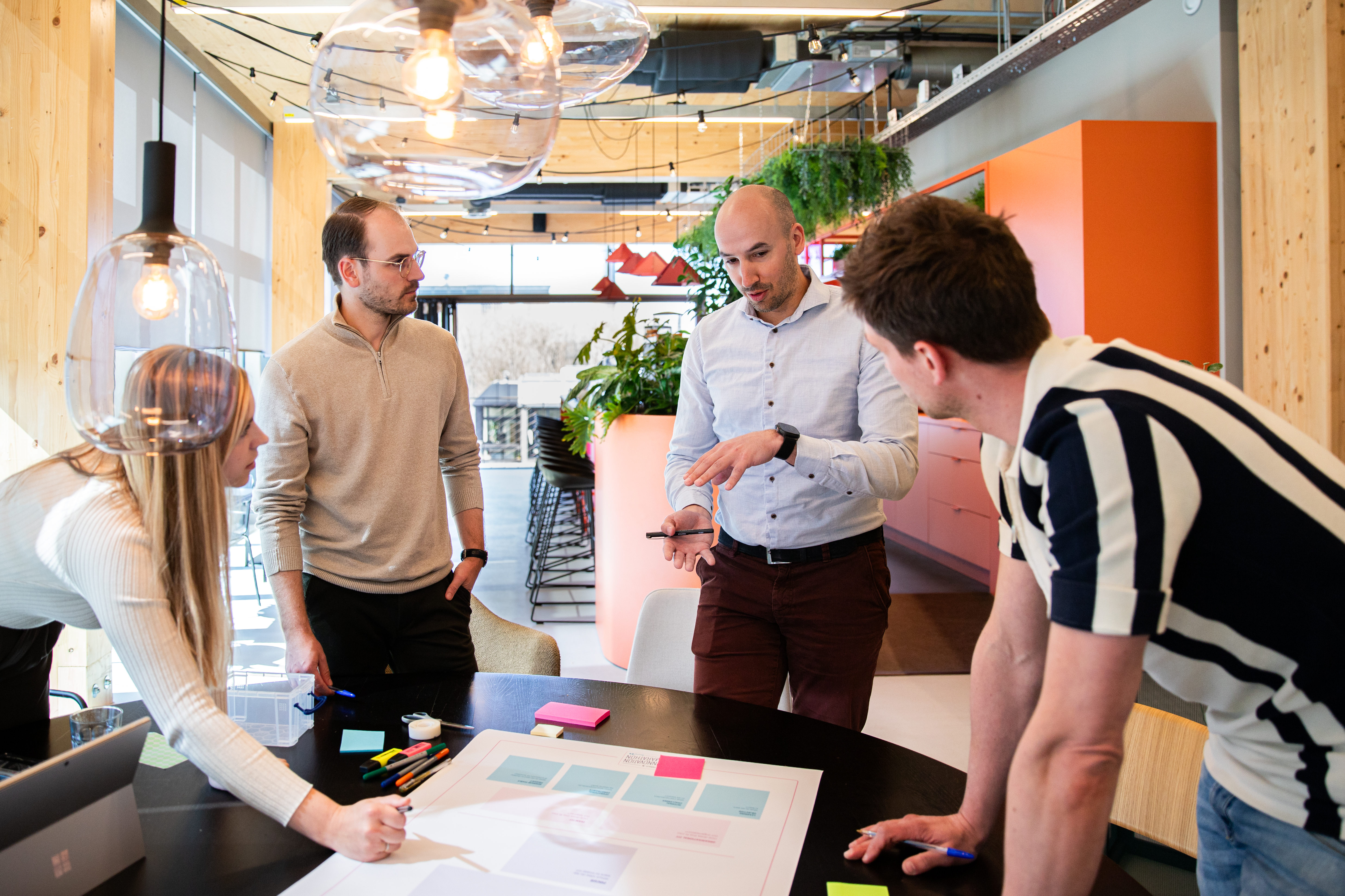 Four people collaborate around sticky notes and an Innovation Marathon board in a modern office.